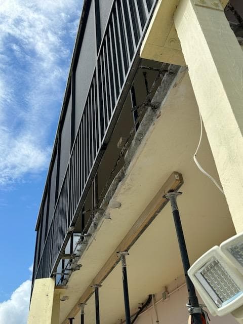 Underside view of balcony showing structural beam repair with temporary supports during spalling restoration in Key West